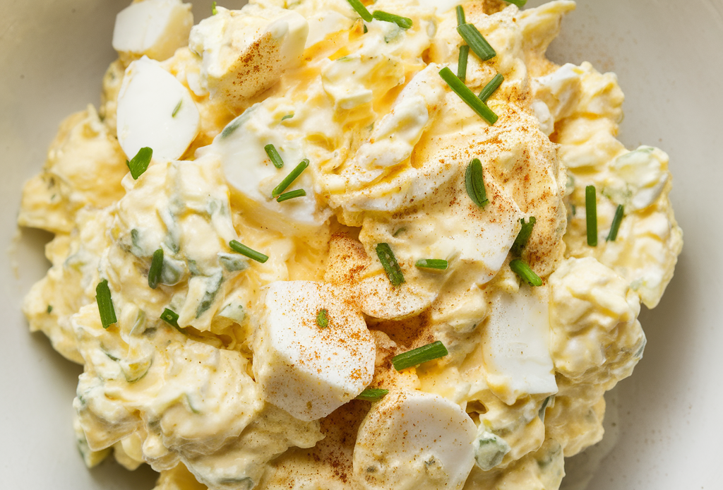 A bowl of creamy egg salad garnished with fresh herbs, served with slices of whole-grain bread and a side of mixed greens.