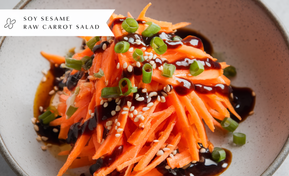 A vibrant bowl of soy sesame raw carrot salad, featuring shredded carrots, sesame seeds, and a light soy dressing, garnished with fresh herbs.
